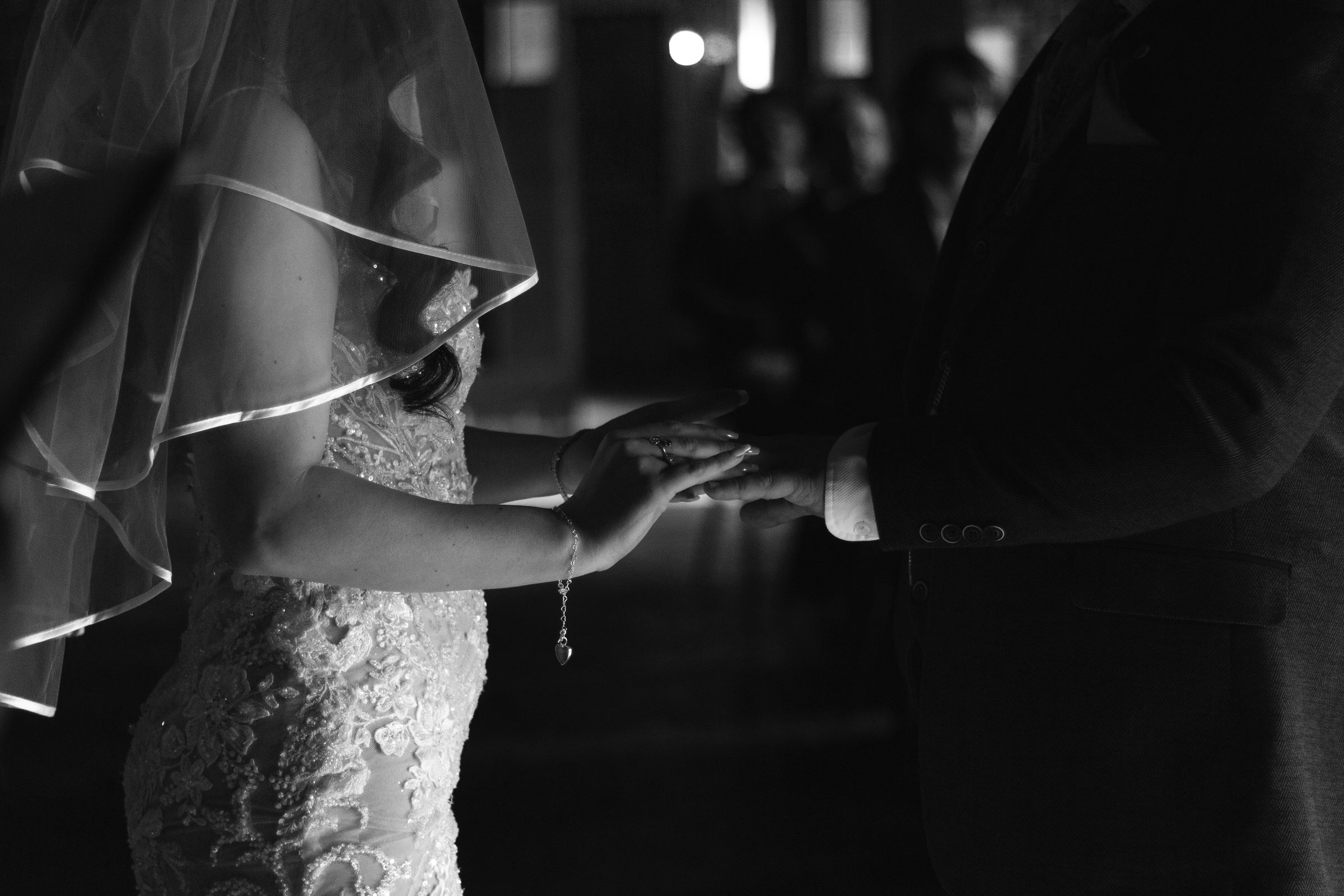 A bride and groom holding hands, seen through a veil, in black and white